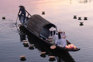 Two beautiful Vietnamese girls in Ao Dai floating lanterns on the Perfume River in Hue, Vietnam.